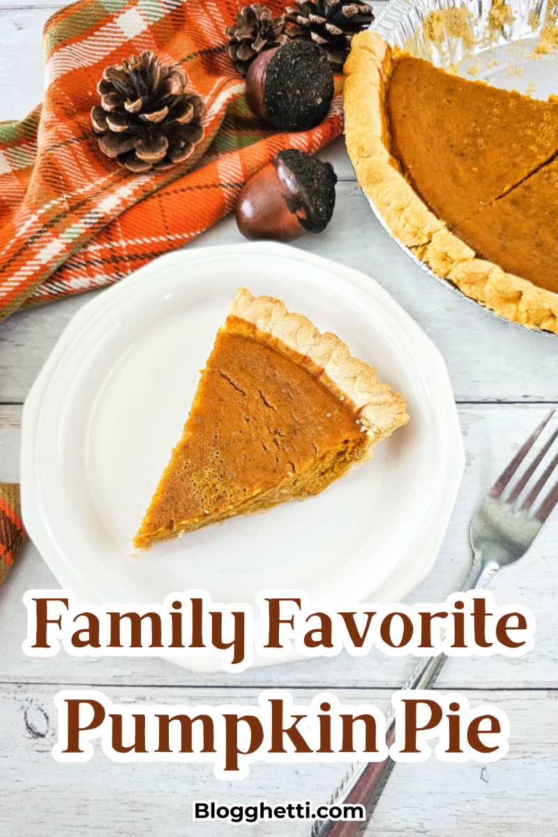 A slice of pumpkin pie on a white plate with the whole pie visible in the background, set on a rustic wooden table. The table is decorated with a colorful orange plaid napkin and autumn decorations including pine cones and acorns. Text overlay states 'Family Favorite Pumpkin Pie' with the website 'Blogghetti.com' mentioned at the bottom.