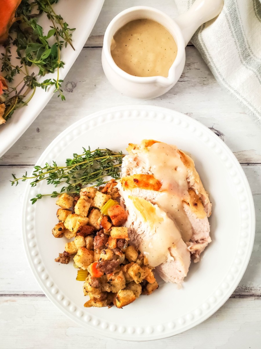 white plate with slice of roasted turkey and stuffing with gravy