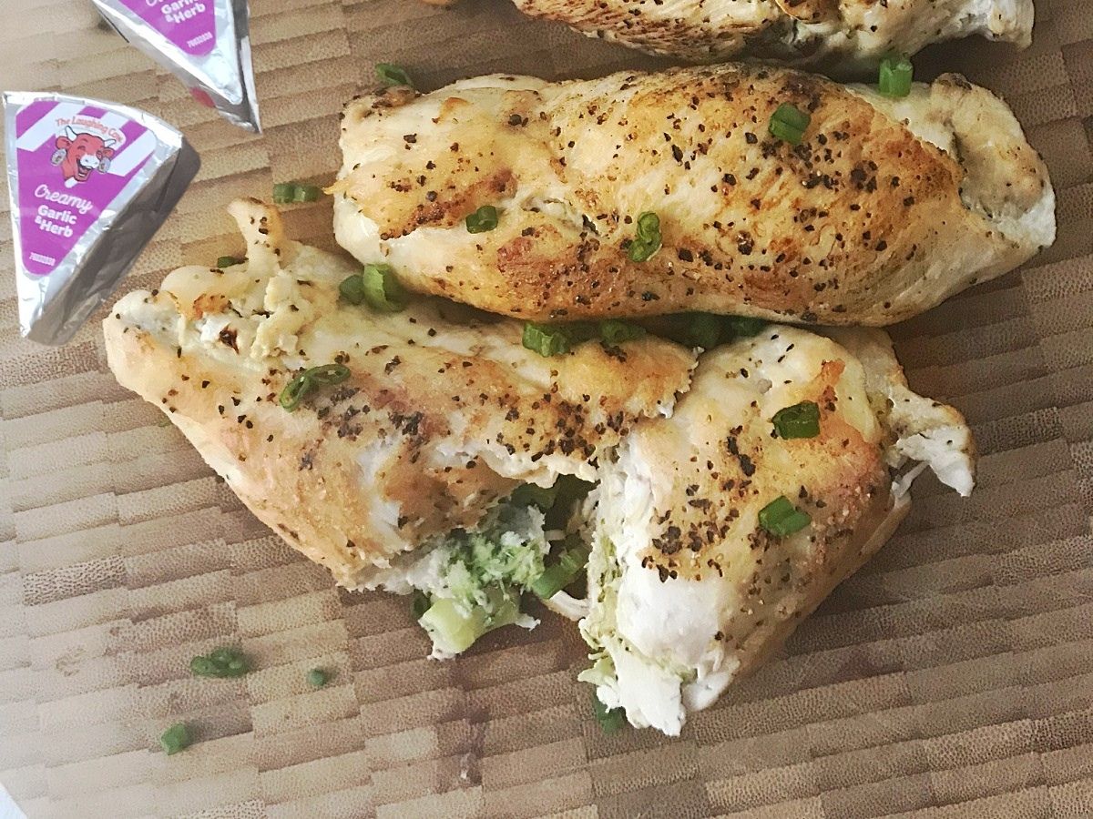 A close-up view of the bottom two stuffed chicken rolls on a wooden board garnished with fresh sliced green onions.