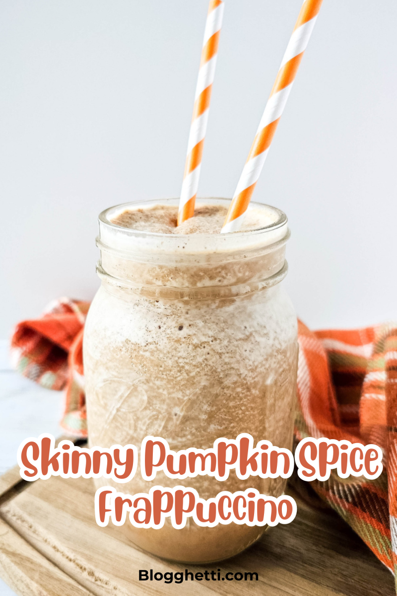 A mason jar filled with a creamy, blended Skinny Pumpkin Spice Frappuccino, topped with a sprinkle of cinnamon. Two orange and white striped straws are placed in the drink, and the jar is set on a wooden surface with an orange plaid cloth in the background. The text 'Skinny Pumpkin Spice Frappuccino' is written in a playful font