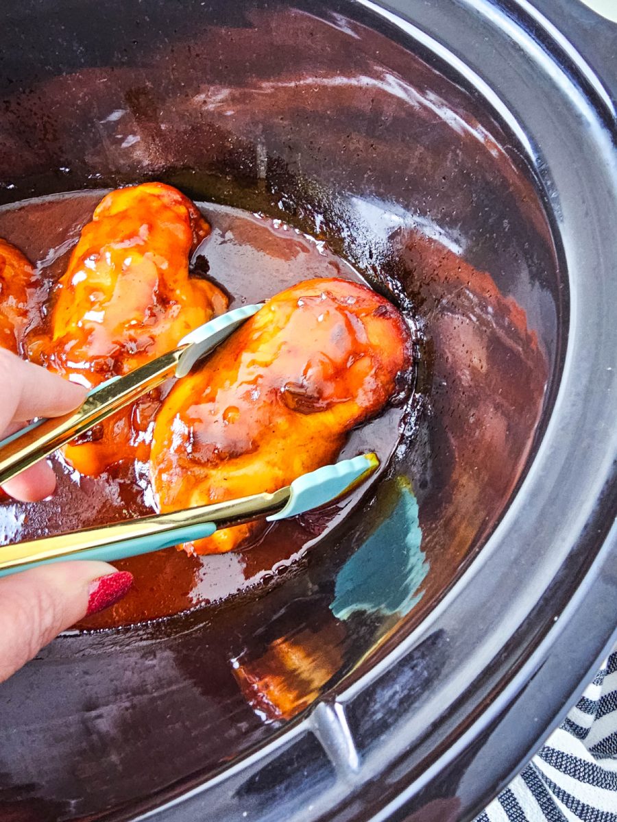 tongs taking a chicken breast from crock pot