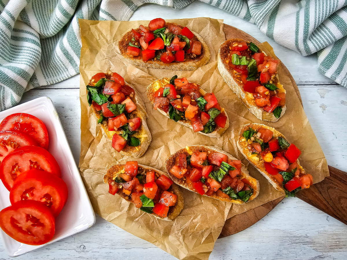 Fresh tomato bruschetta arranged on a wooden board with sliced tomatoes on the side.