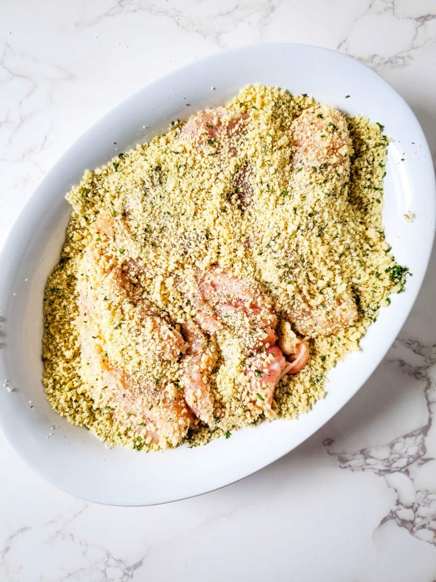 adding panko bread crumbs to the chicken breasts in shallow bowl