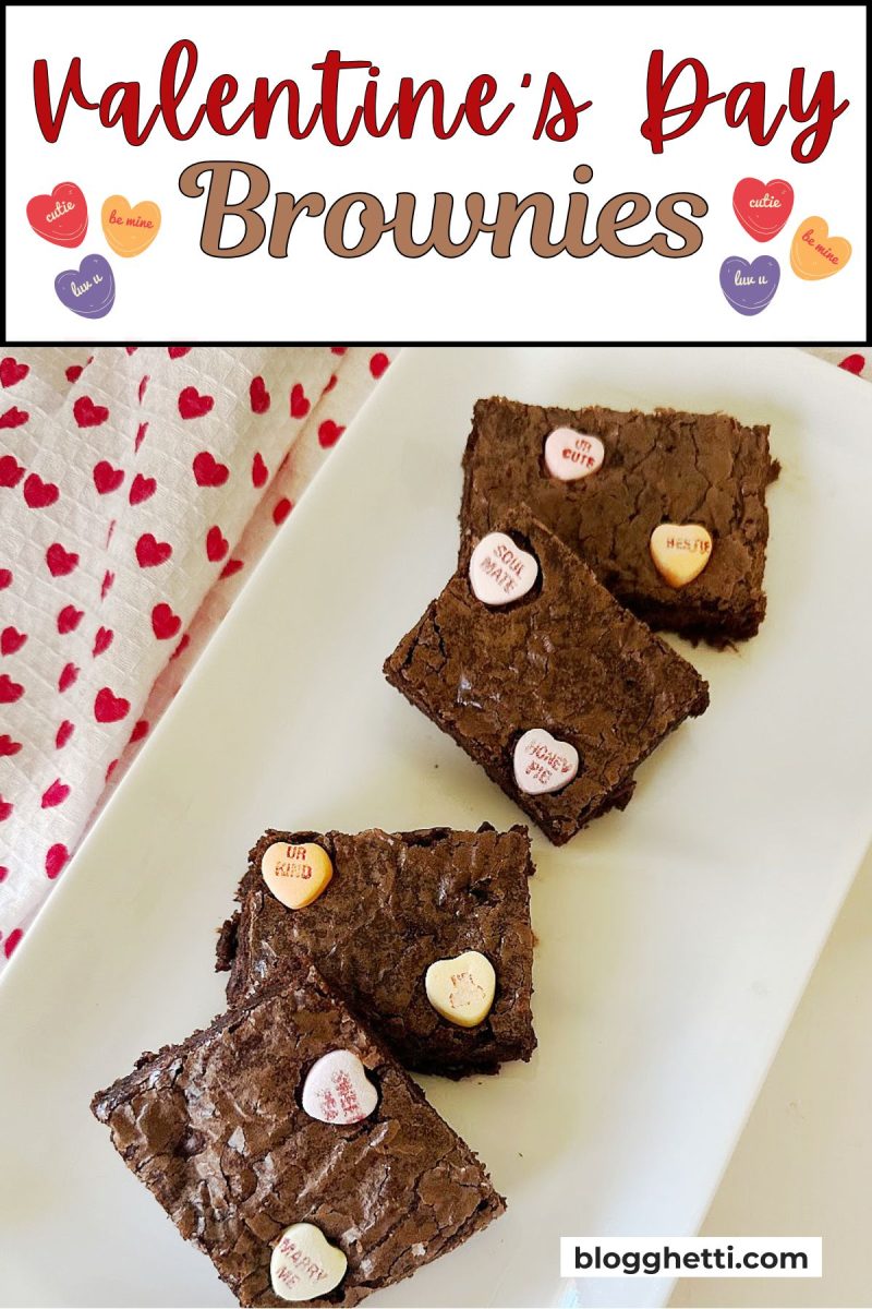 Easy Valentine's Day Brownies | Blogghetti A group of four chocolate squares topped with pastel conversation heart candies, arranged on a long white rectangular plate. A white cloth with red hearts sits to the left. The top of the image features a white banner with the title "Valentine’s Day Brownies" in decorative red and brown text, flanked by small heart graphics.