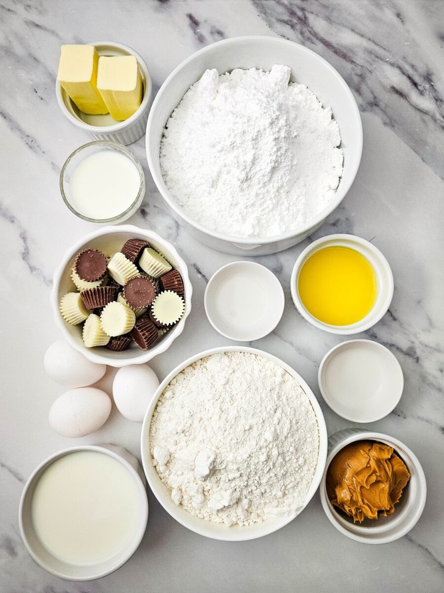 Overhead arrangement of cake mix, powdered sugar, butter, milk, eggs, vanilla, peanut butter, and milk chocolate and white chocolate peanut butter cups.