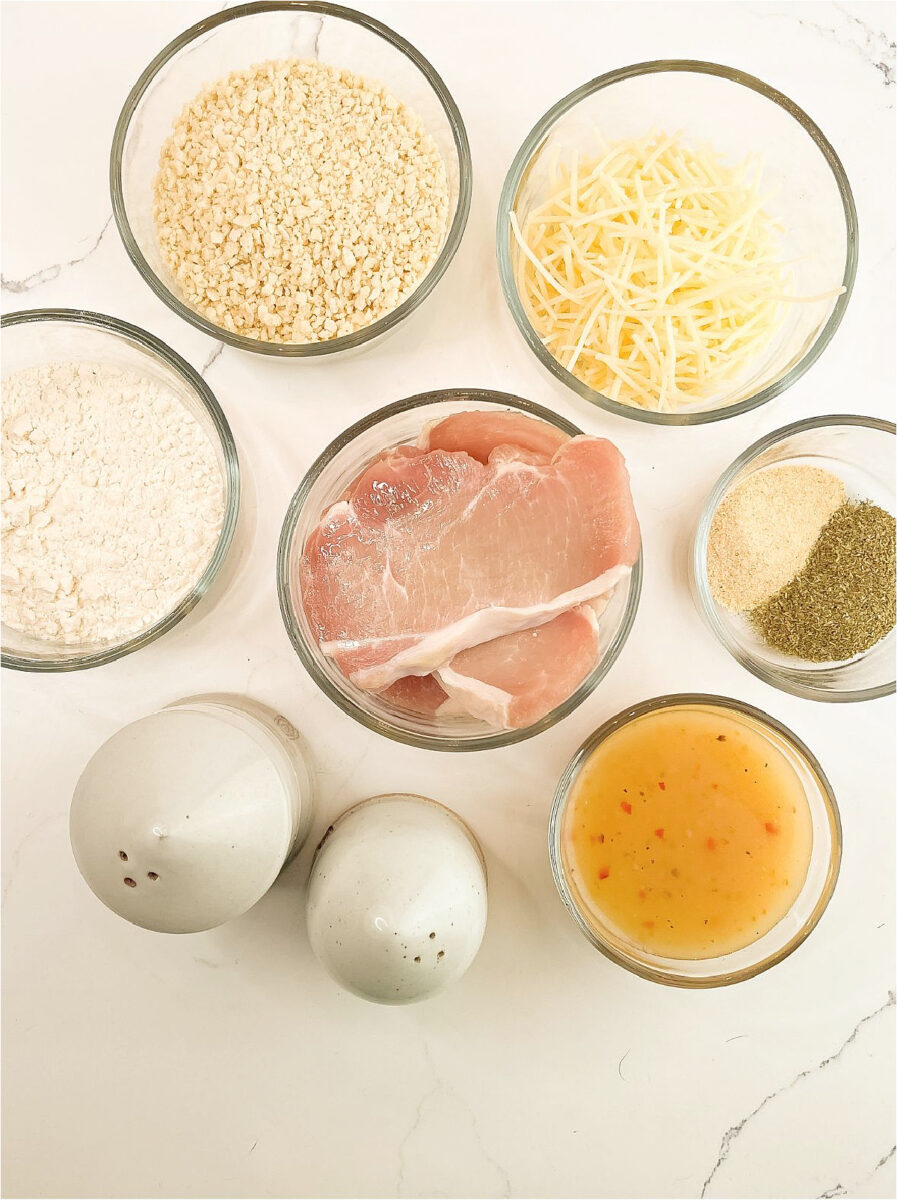 Ingredients for crispy baked pork chops, including boneless pork chops, Italian dressing, breadcrumbs, Parmesan cheese, flour, and seasonings.