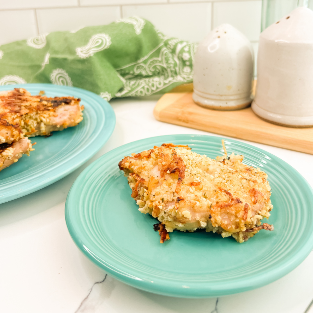 Italian Baked Pork Chops served on turquoise plates, with one crispy breaded pork chop in the foreground and two more on a second plate in the background.