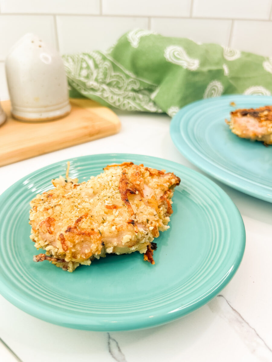 Breaded pork chop with a crisp golden crust served on a turquoise plate with another plate blurred in the background.