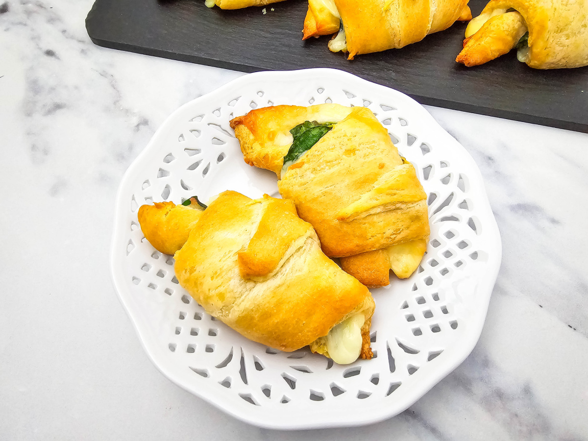 Two golden-brown spinach and cheese crescent rolls are placed on a decorative white plate.