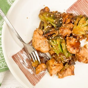 A skillet chicken and broccoli dinner on a white plate, with a fork resting on the side, highlighting the textured chicken and vibrant broccoli florets.
