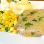 Plate of slow cooked Italian pork chops garnished with parsley, served with mashed potatoes and corn