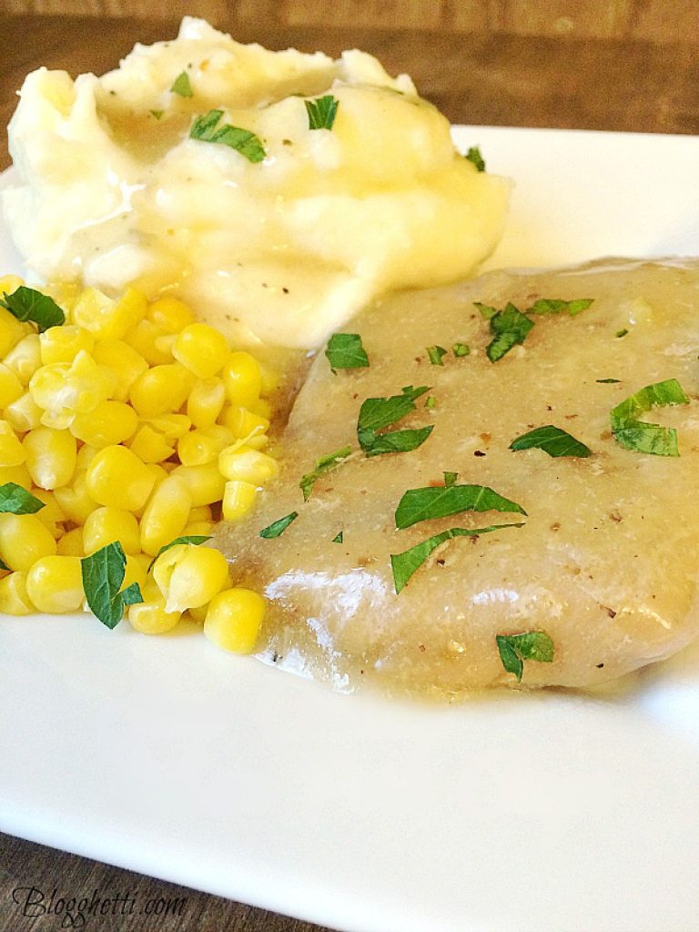 Plate of slow cooked Italian pork chops garnished with parsley, served with mashed potatoes and corn