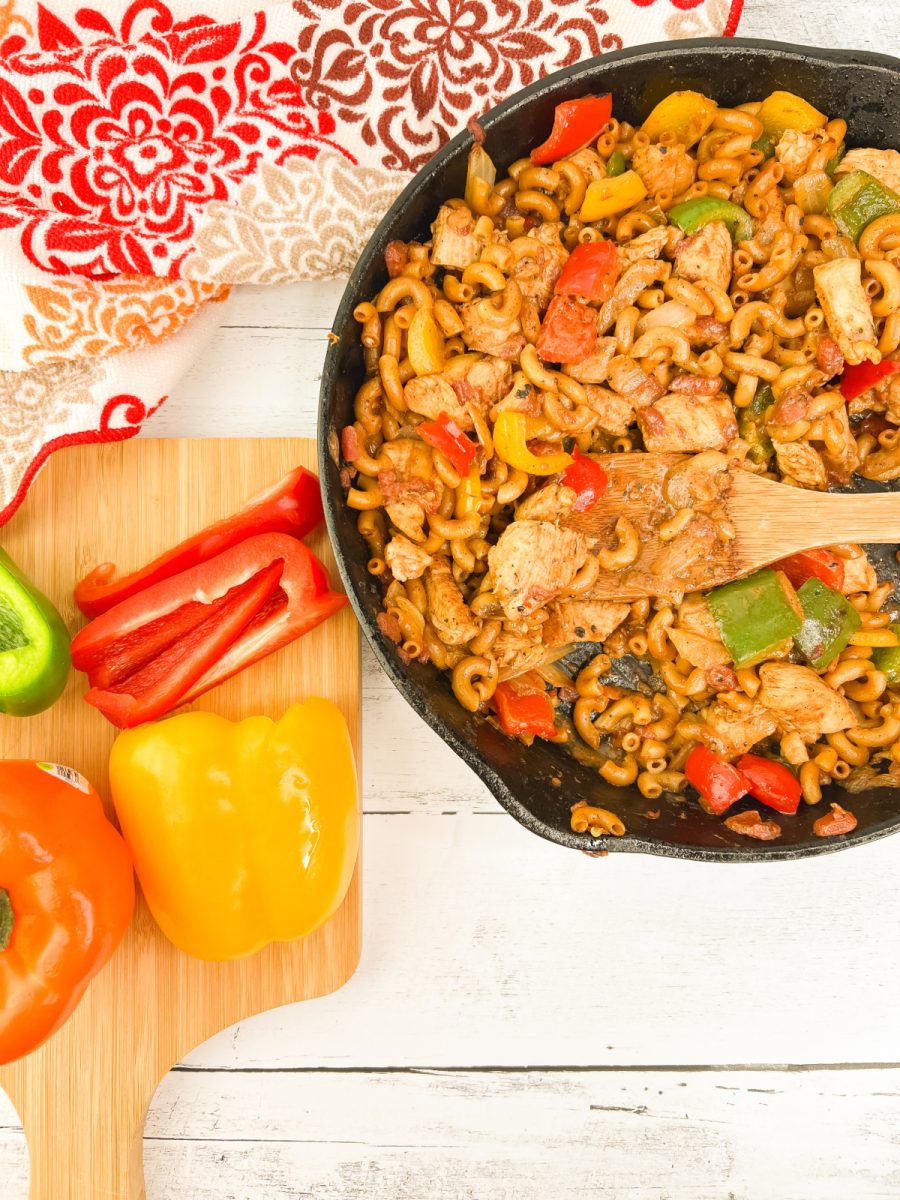 A top-down look at a finished skillet meal featuring elbow macaroni coated in a zesty cream sauce with chicken and peppers.