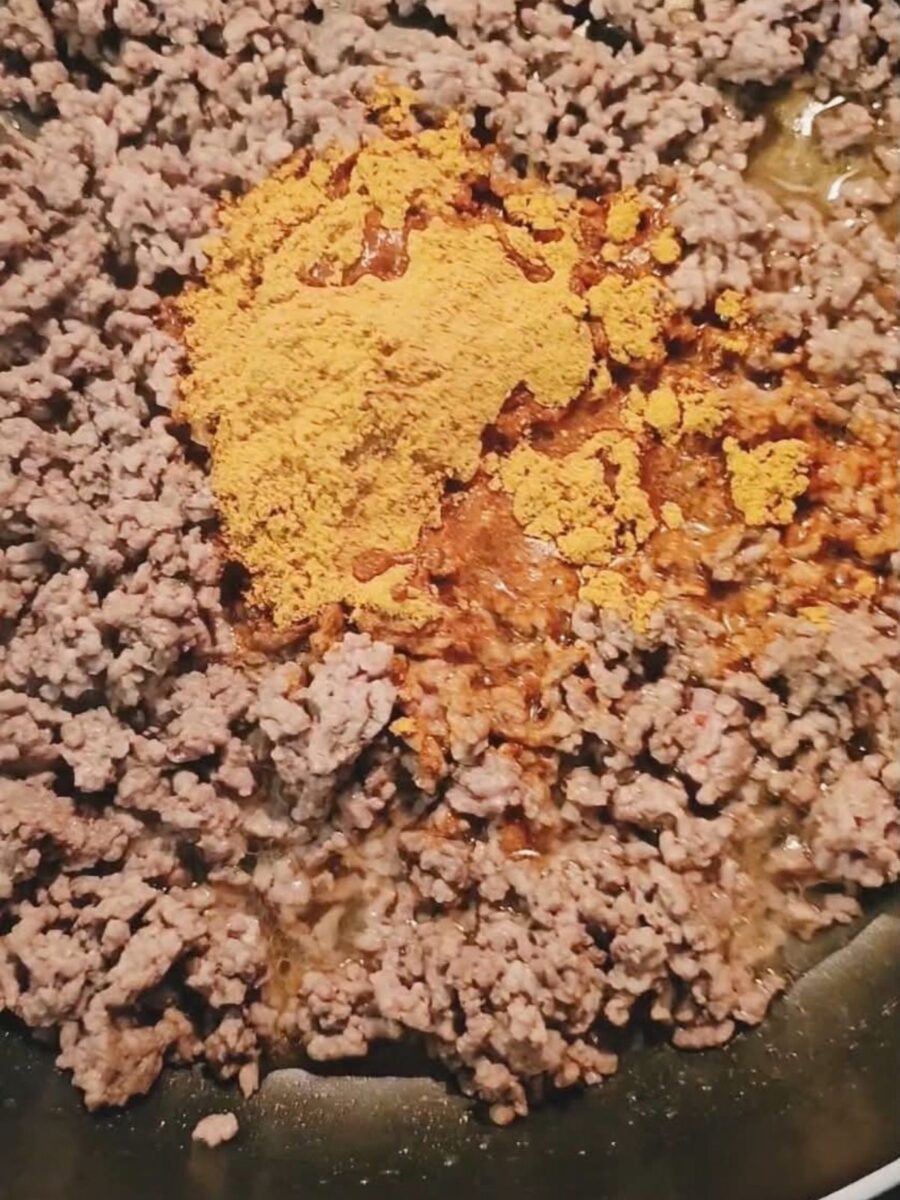 Taco seasoning and water added to browned ground beef in a skillet before stirring.