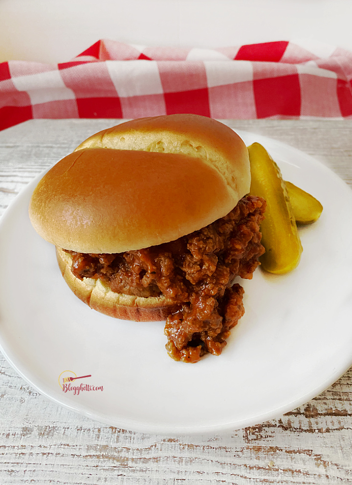 white plate with sloppy joe sandwich and pickle