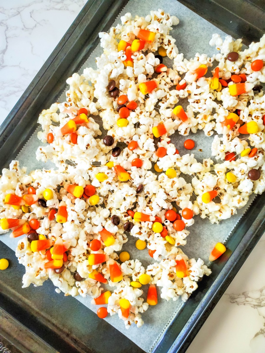 adding the candy to popcorn mixture on baking sheet