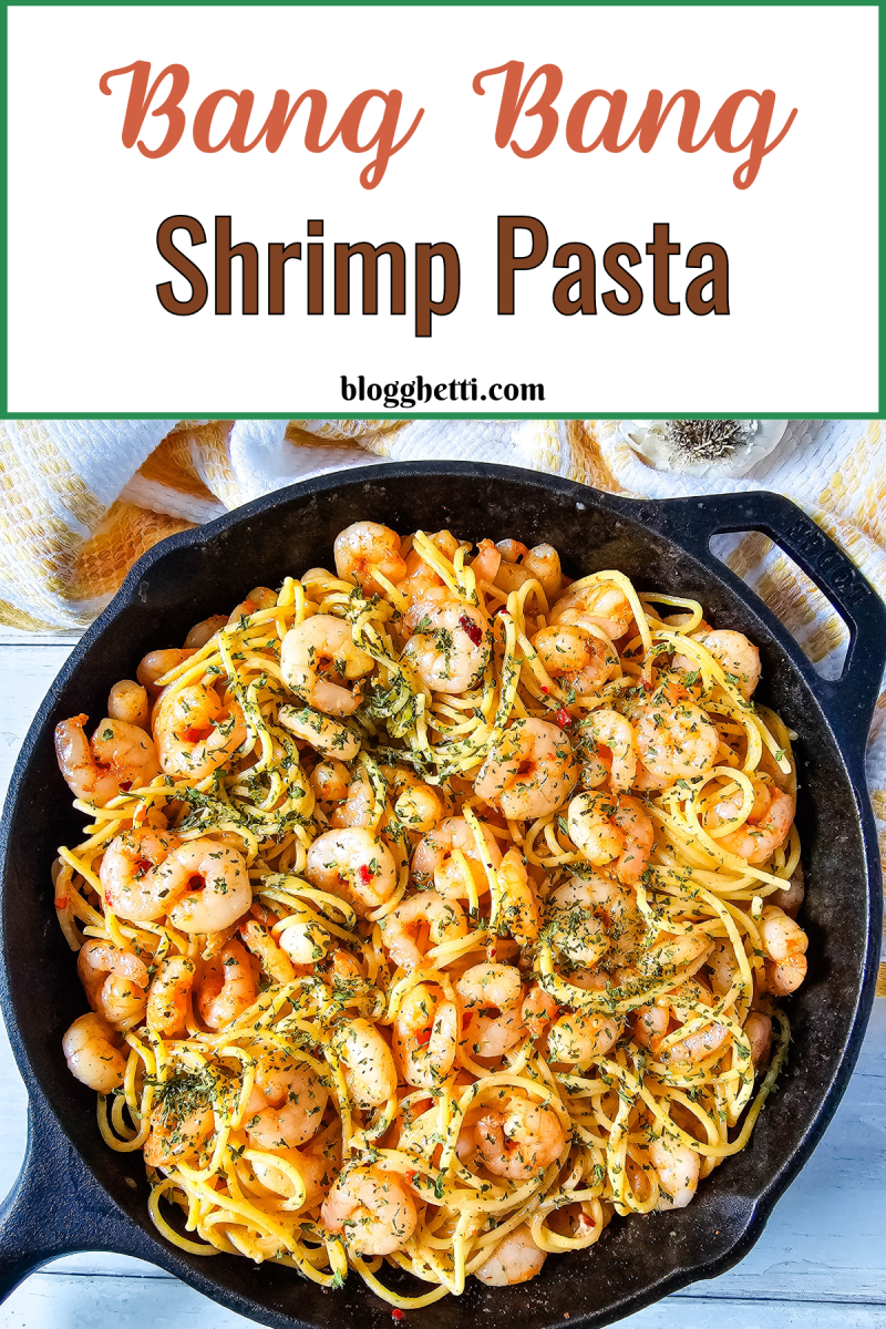 A close-up of a cast iron skillet filled with Bang Bang Shrimp Pasta. The dish features golden, sautéed shrimp mixed with pasta, coated in a creamy, spicy sauce, and garnished with herbs. The shrimp are plump and lightly browned, while the pasta is evenly coated, creating a vibrant, appetizing look. Above the image, the text reads "Bang Bang Shrimp Pasta" in a bold, stylish font. The skillet sits on a light-colored surface with a yellow and white towel in the background.