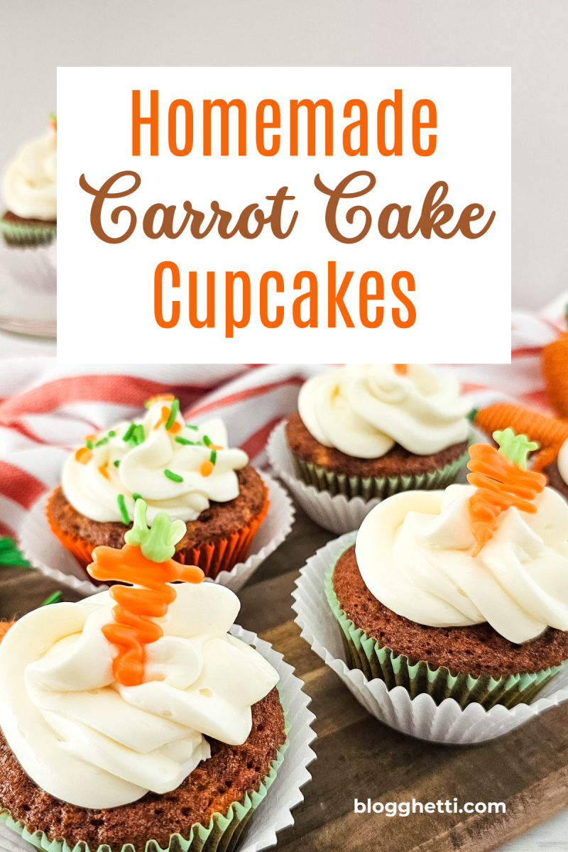 Close-up of decorated carrot cake cupcakes with white frosting and orange carrot accents, displayed on a wooden board with a red and white cloth.