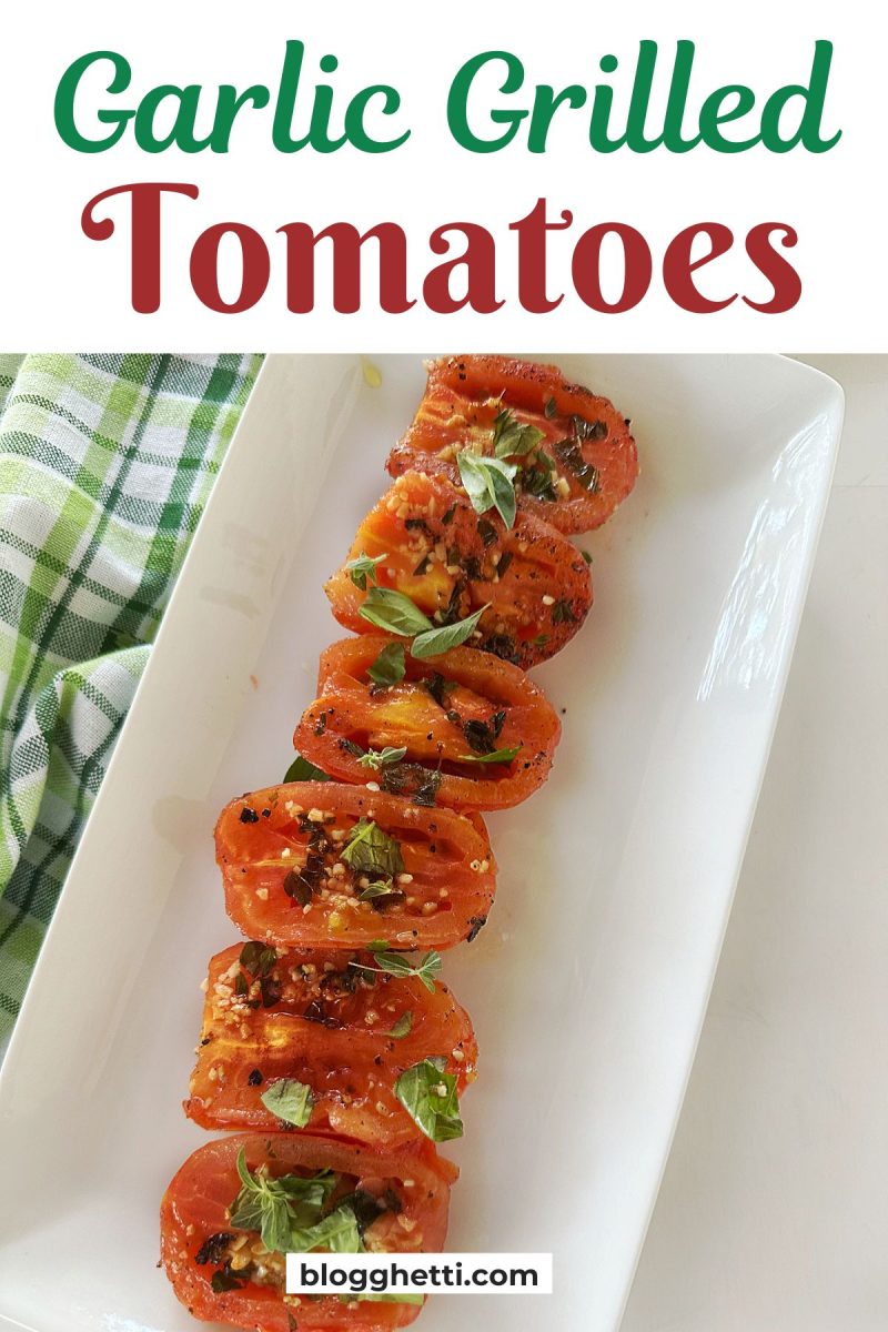 Grilled tomato halves seasoned with garlic and herbs on a white rectangular plate.