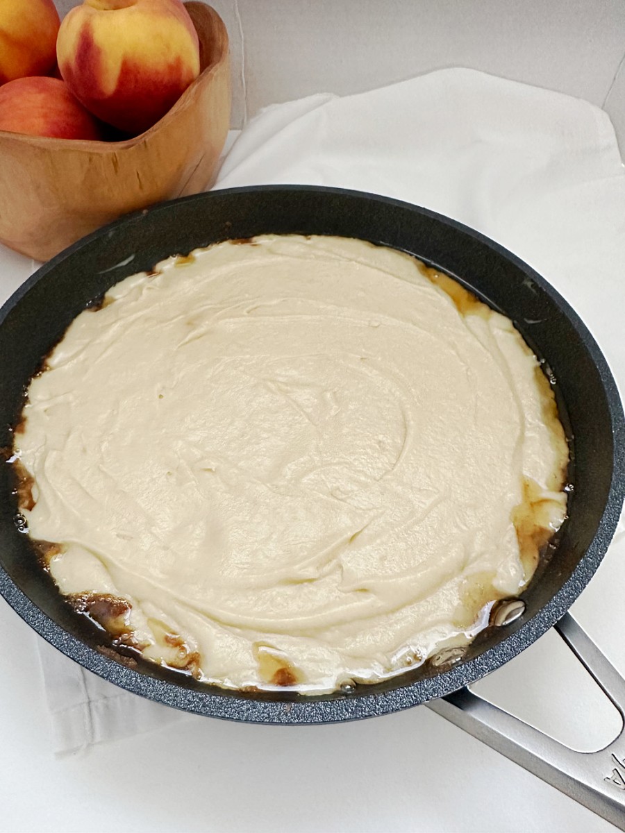 cake batter on top of peaches in skillet ready to bake