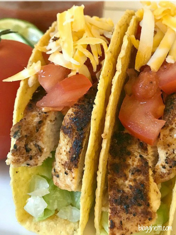 two hard shelled grilled chicken tacos with lettuce, tomatoes and cheese on them