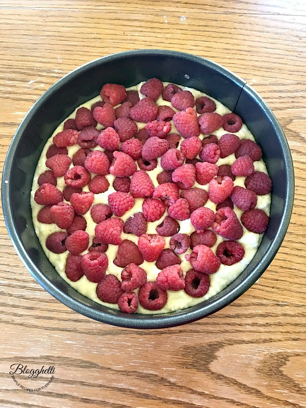 Pan with lemon cake batter topped with raspberries