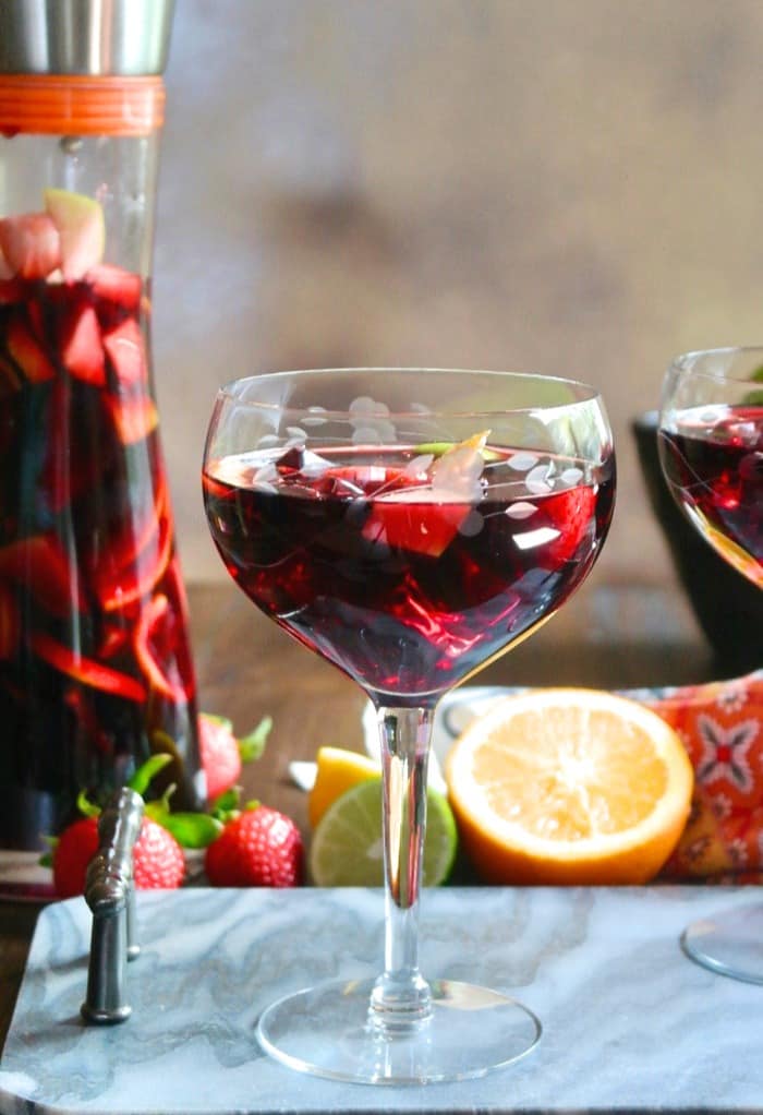 Spanish Sangria in a wine glass with fruit in it. Carafe of Spanish Sangria beside the glass