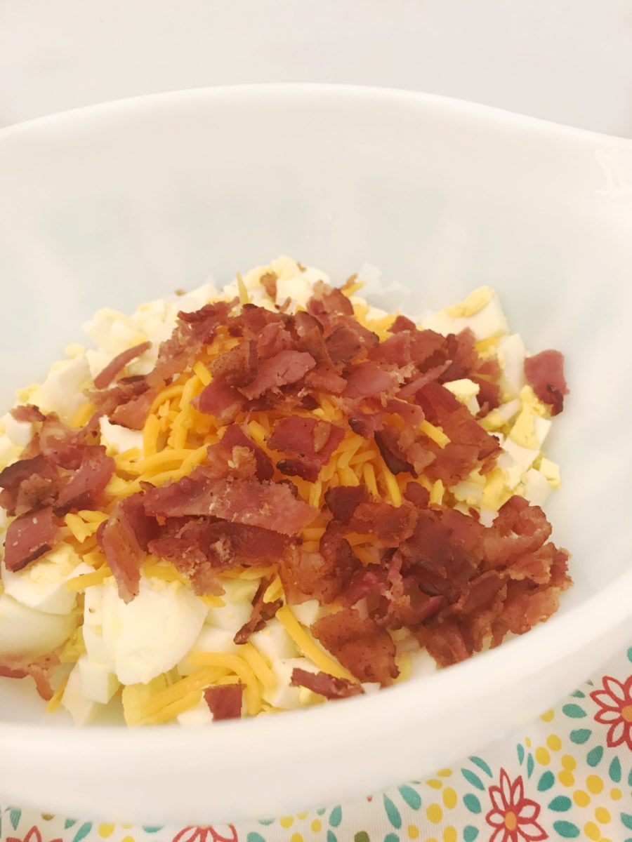 bacon and cheese added to egg salad in white bowl