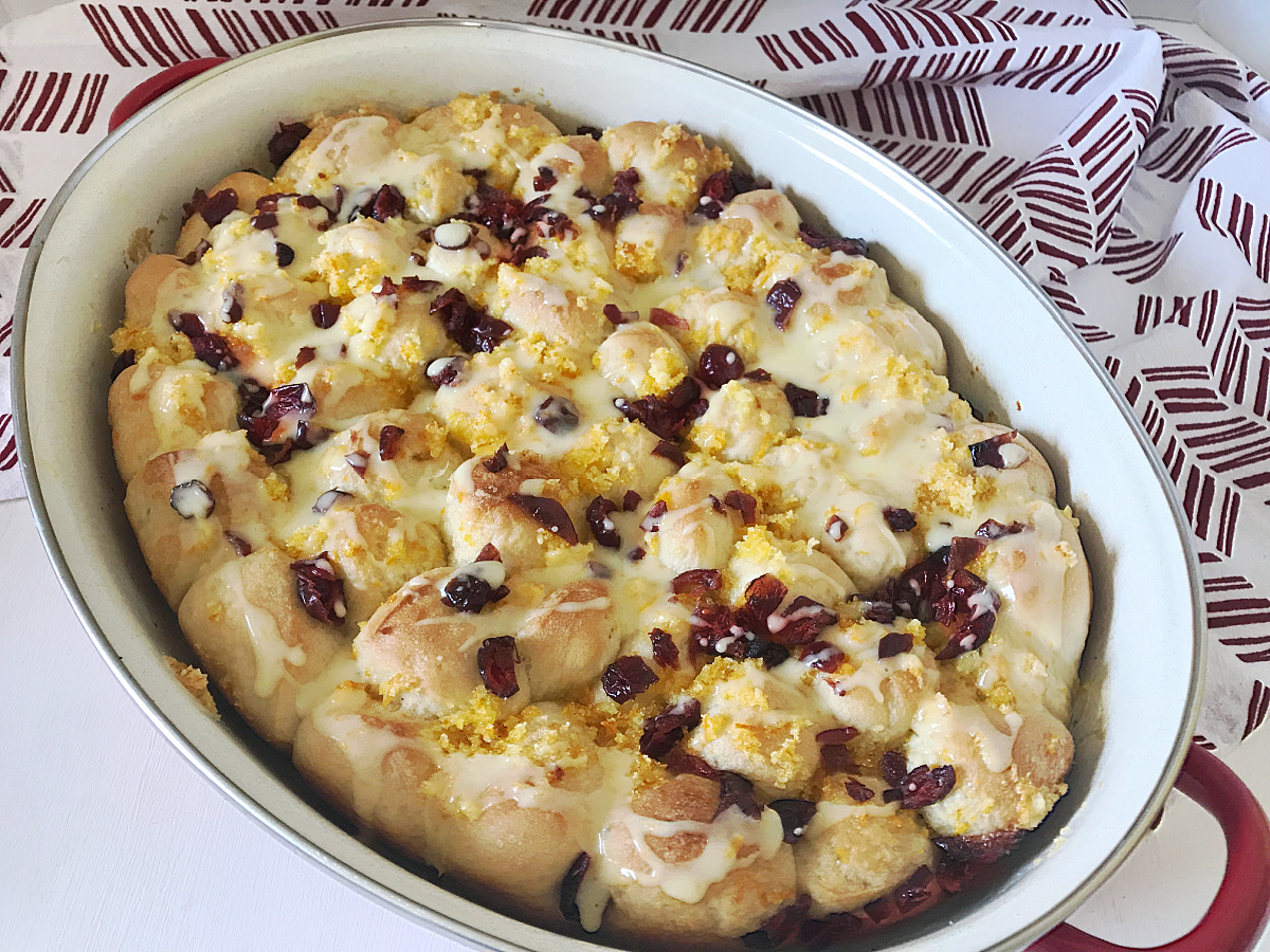 Red and White baking dish filled with glazed breakfast bread topped with chopped dried cranberries and orange sugar.