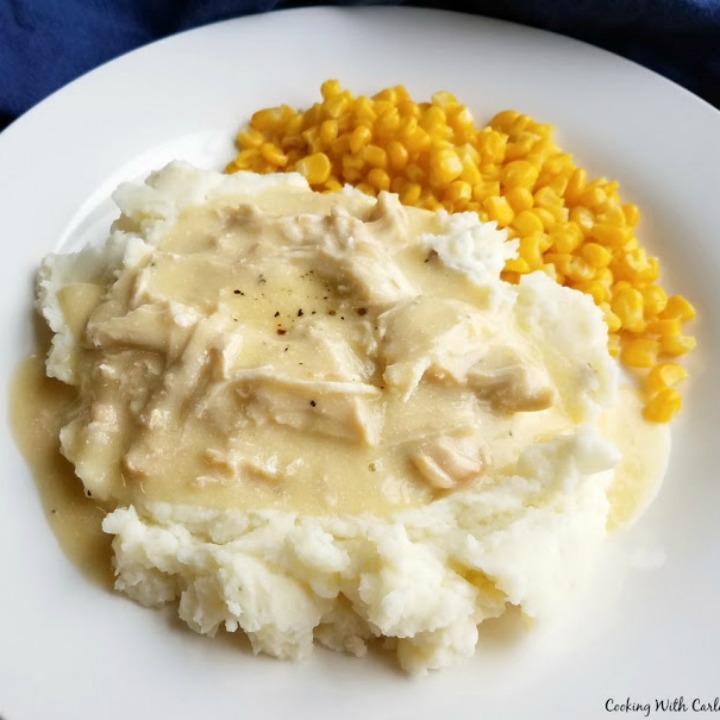 Creamy Chicken and Gravy over mashed potatoes with corn on the side on a white plate