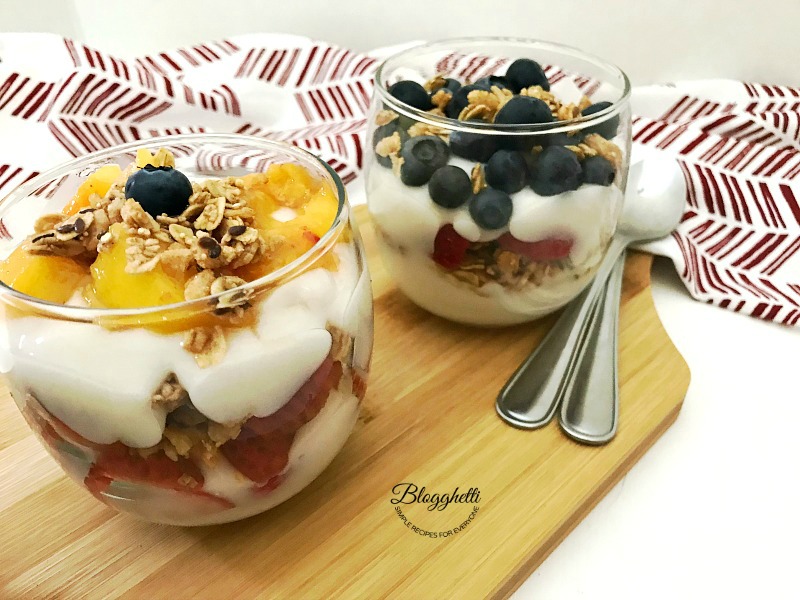 Fresh Fruit and yogurt in dessert glasses on a wooden board with spoons
