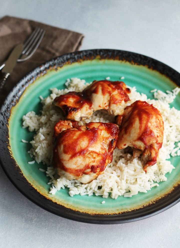 Baked chicken thighs over rice on teal plate