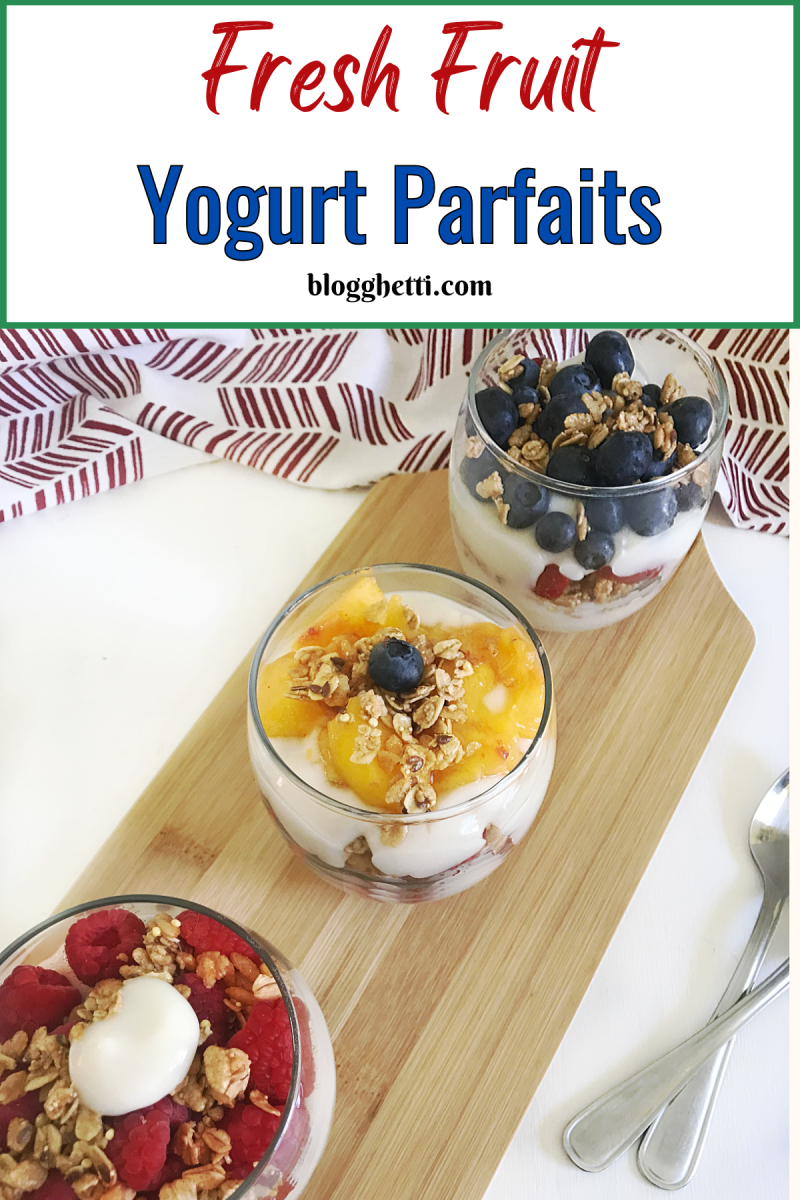 Three glass bowls filled with yogurt parfaits on a wooden cutting board. Each parfait is layered with yogurt, fresh fruit (raspberries, blueberries, peaches), and granola.