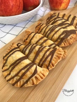 Chocolate Glazed Apple Hand Pies on a wooden platter with apples in the background