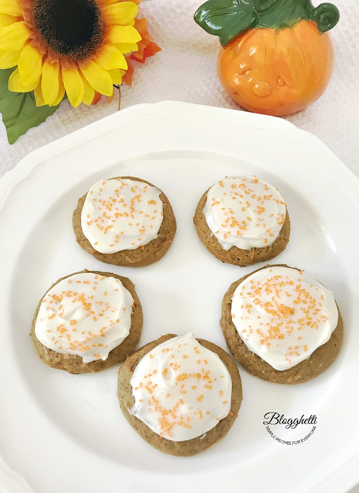 Pumpkin Cookies with Cream Cheese Frosting on a white plate with pumpkin and sunflower in background