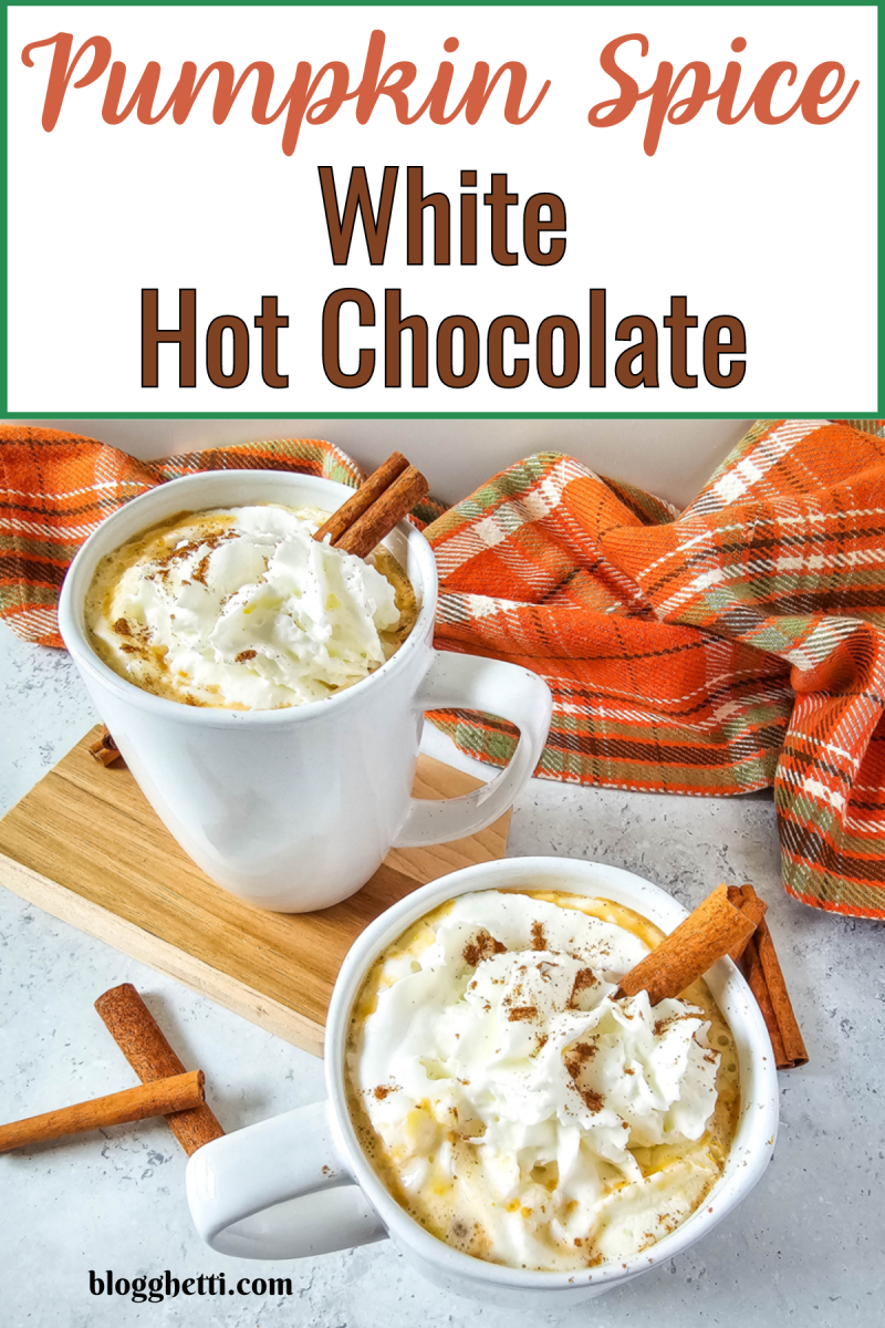 Two cozy mugs of Pumpkin Spice White Hot Chocolate topped with whipped cream, sprinkled with pumpkin spice, and garnished with cinnamon sticks. The mugs are placed on a wooden board against a backdrop of an orange and green plaid blanket, giving the image a warm and festive autumn vibe. The image has a text overlay that reads 'Pumpkin Spice White Hot Chocolate' at the top