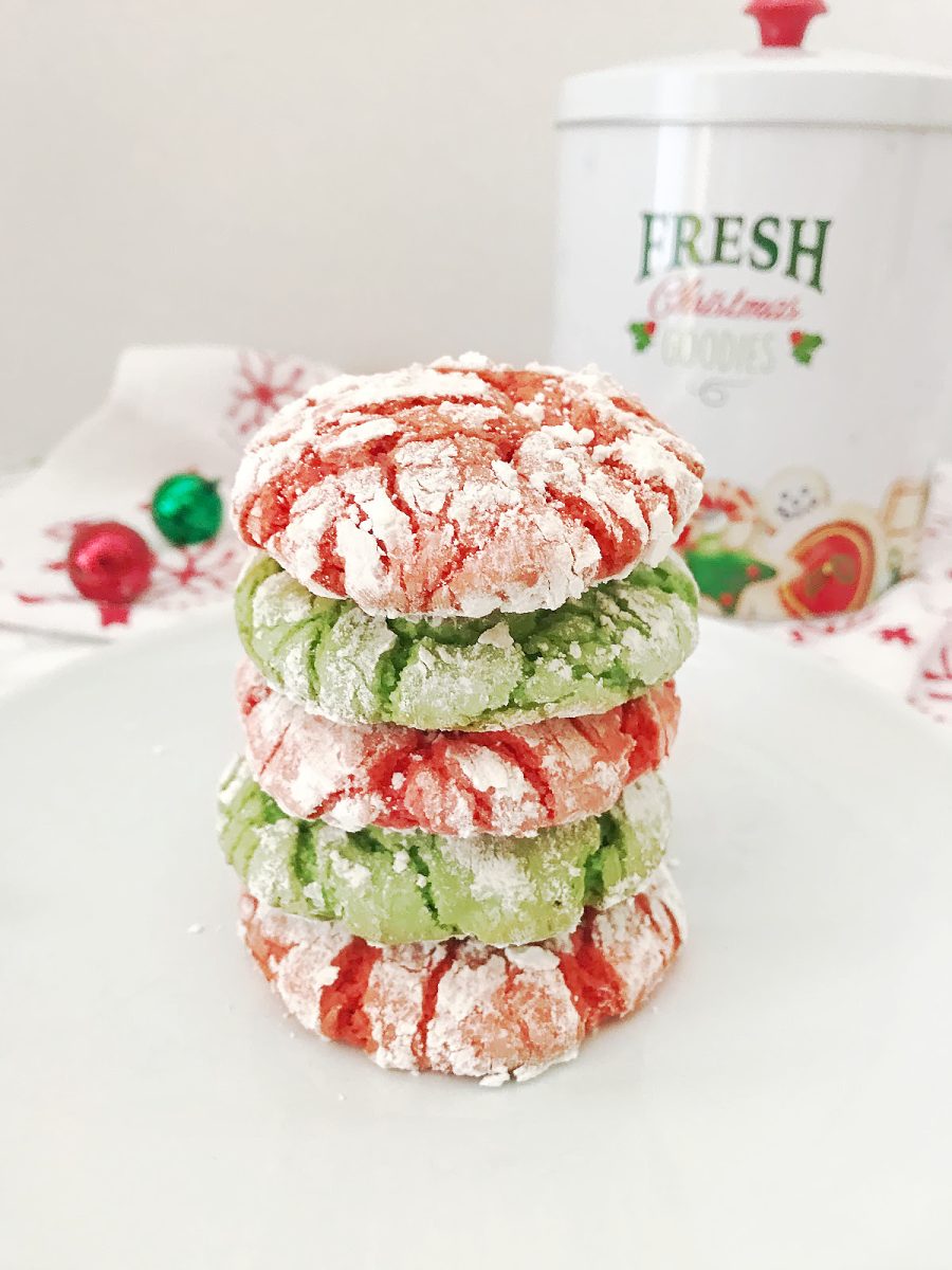 Stack of four baked red and green crinkle cookies covered in powdered sugar on a white plate, with a white Christmas treat canister visible in the background.