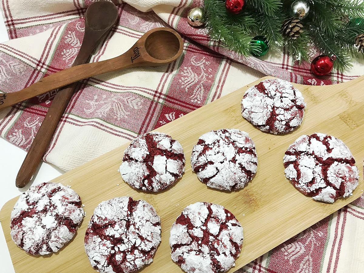 A top-down view of Red Velvet Crinkle Cookies arranged on a wooden board with Christmas ornaments and evergreen sprigs in the background.