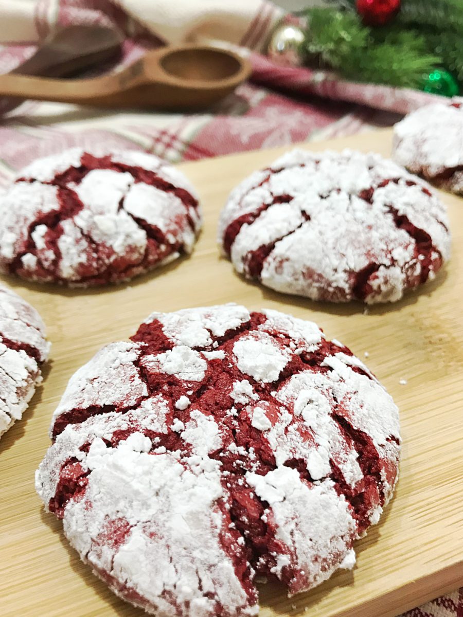 Close-up of Red Velvet Crinkle Cookies on a wooden board, with a blurred festive background including Christmas decorations.