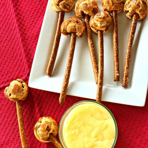 plate of mini cinnamon rolls on pretzel stick and a bowl of cinnamon roll dip