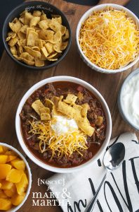 bowl of sweet and sassy chili with bowls of chili toppings like cheese, peaches and more