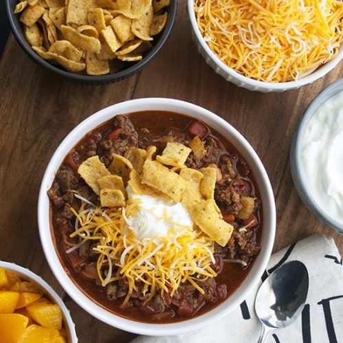 bowl of sweet and sassy chili with bowls of chili toppings like cheese, peaches and more