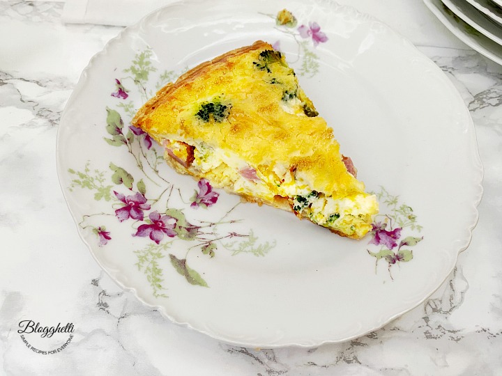 singular slice of broccoli and ham quiche on a white flowered plate