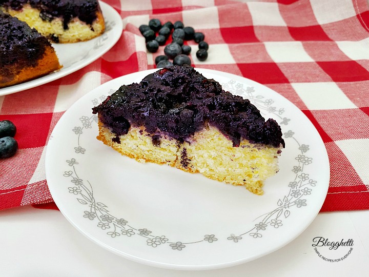 a slice of blueberry upside down cake on white plate with red checkered towel