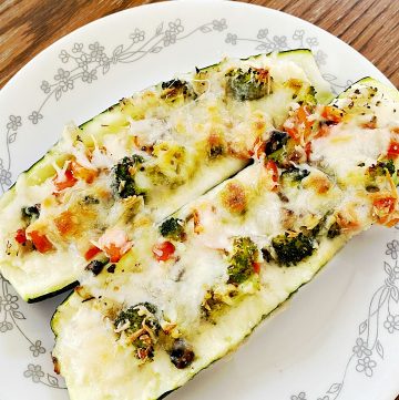 Three cheese stuffed zucchini with veggies on a while plate