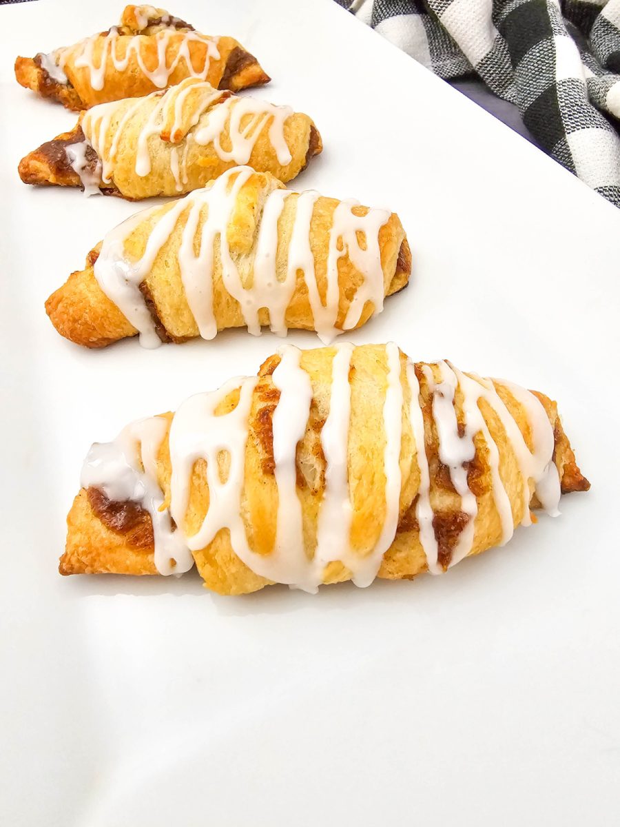  Four golden-baked pumpkin crescent pastries, drizzled with a white icing glaze, are arranged on a long white platter. A black and white checkered napkin is visible in the upper right corner.
