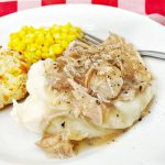 chicken and gravy with mashed potatoes, corn and cheese biscuit on white plate