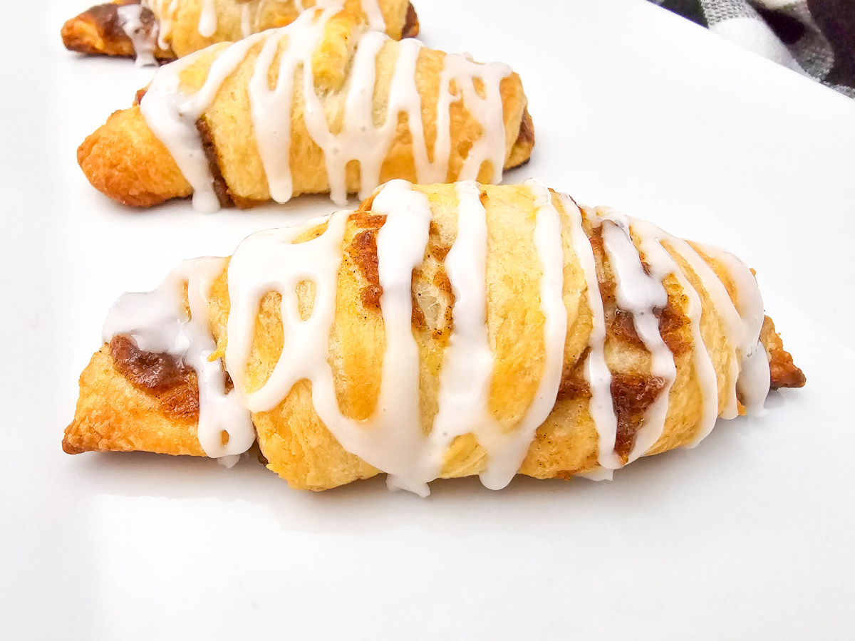 A close-up view of a single golden-baked pumpkin pie pastry, generously drizzled with white icing, resting on a white platter.
