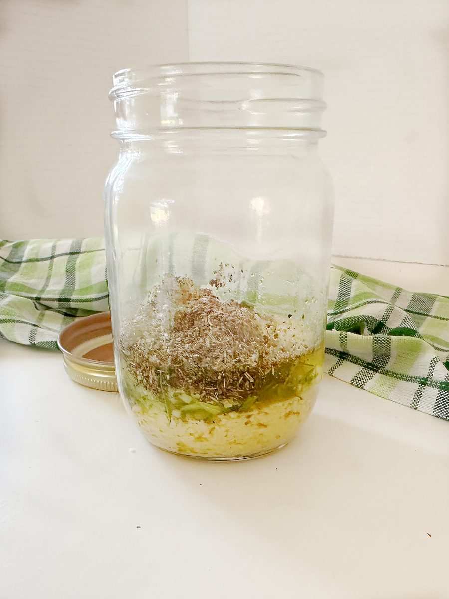  All of the dressing ingredients, including olive oil, Dijon mustard, and fresh rosemary, are added to a mason jar and ready to be mixed.