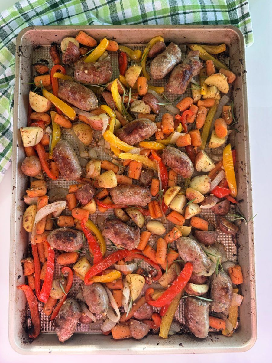 Overhead shot of a sheet pan with roasted Italian sausage, carrots, potatoes, and bell peppers garnished with fresh rosemary.